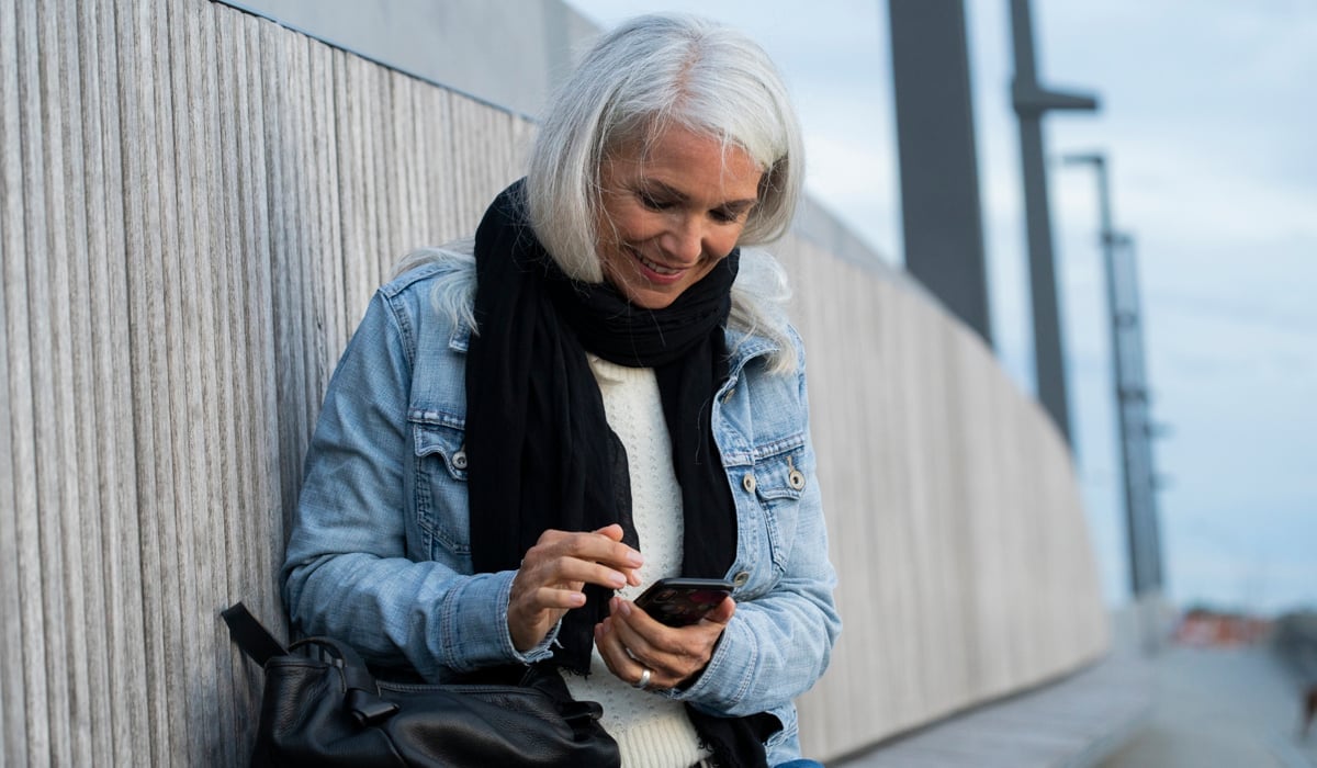 En kvinna sitter på en vägg och tittar på sin mobiltelefon.